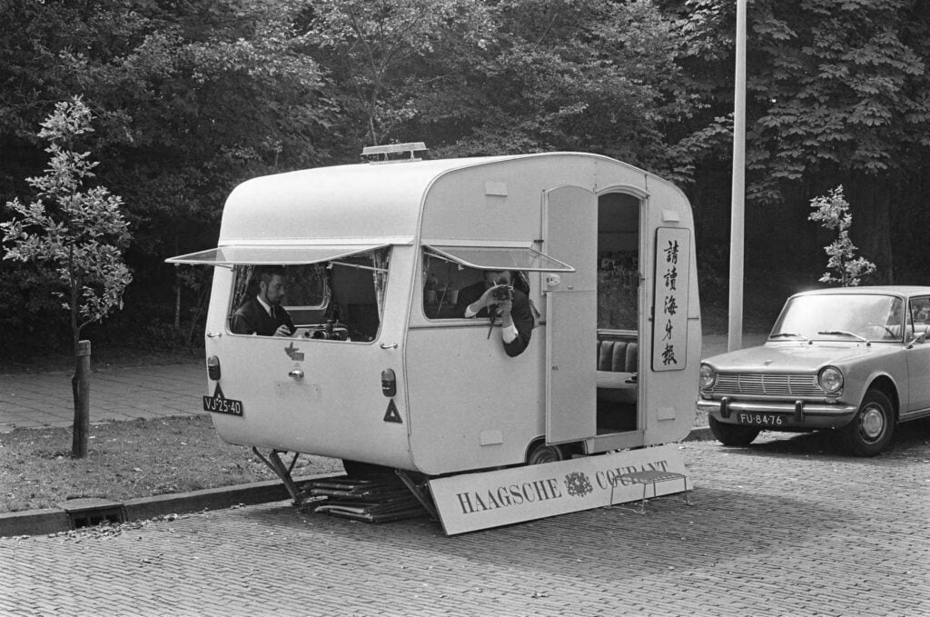 Een verslaggever en een fotograaf van de Haagsche Courant posten bij de ambassade in een caravan