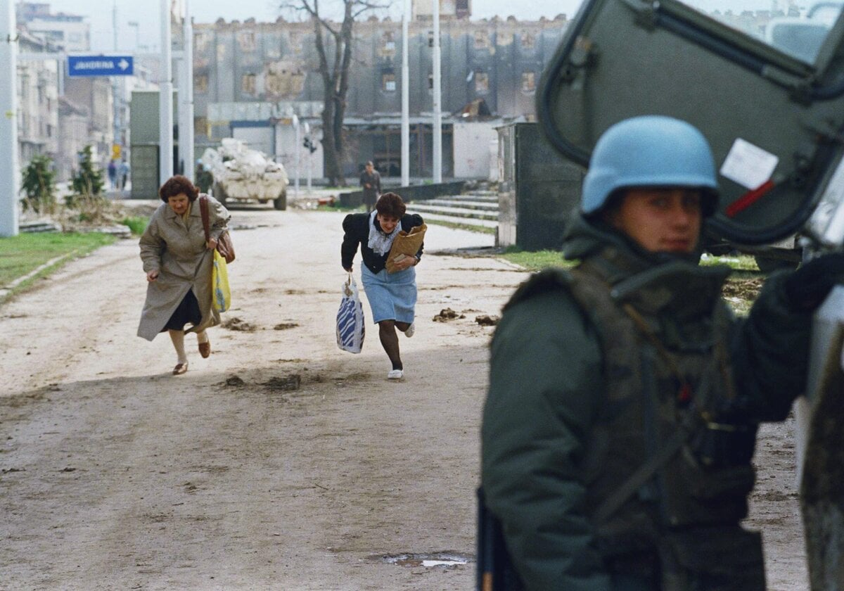 Inwoners van Sarajevo rennen over sniper alley terwijl een VN-soldaat toekijkt.