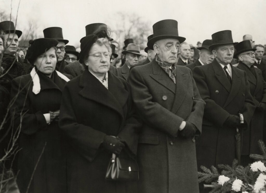 Plechtige gezichten tijdens een begrafenis in 1951.