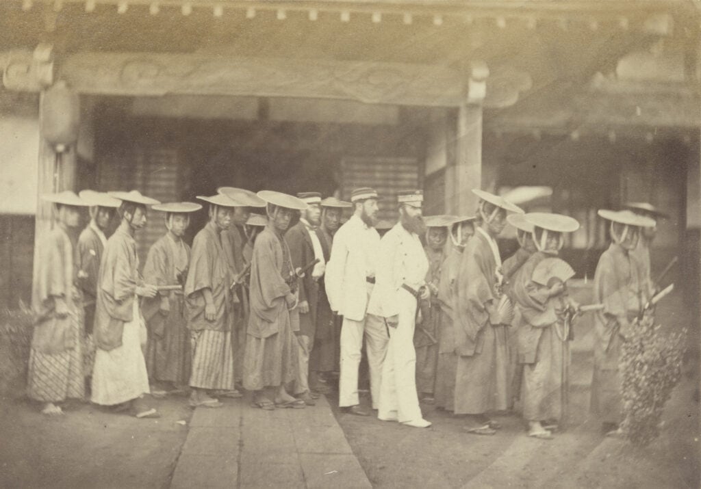Dirk de Graeff van Polsbroek (in wit pak met lange baard) wordt begeleid door een Japanse escorte in Edo. Foto door Felice Beato, 1863.