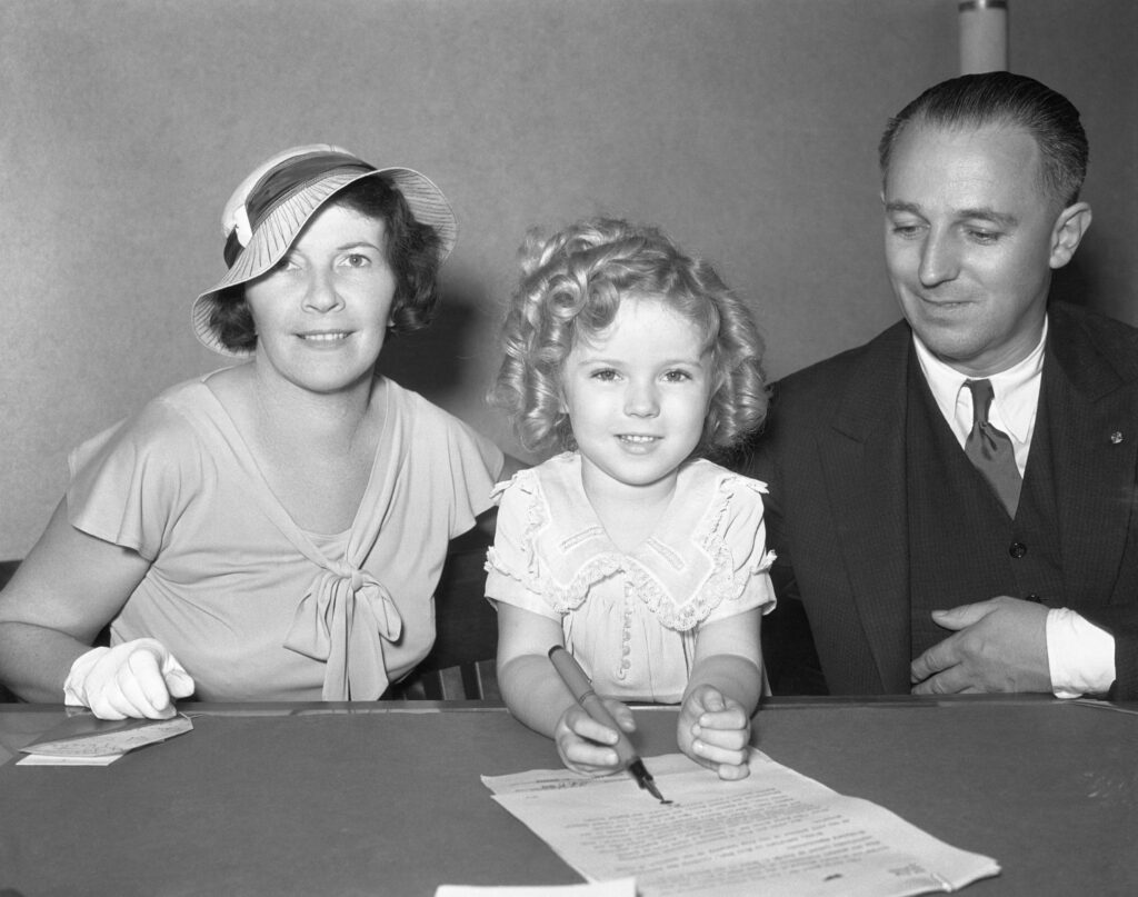 Shirley tekent een contract, geflankeerd door haar ouders Getrude en George Temple, 21 juli 1934.
