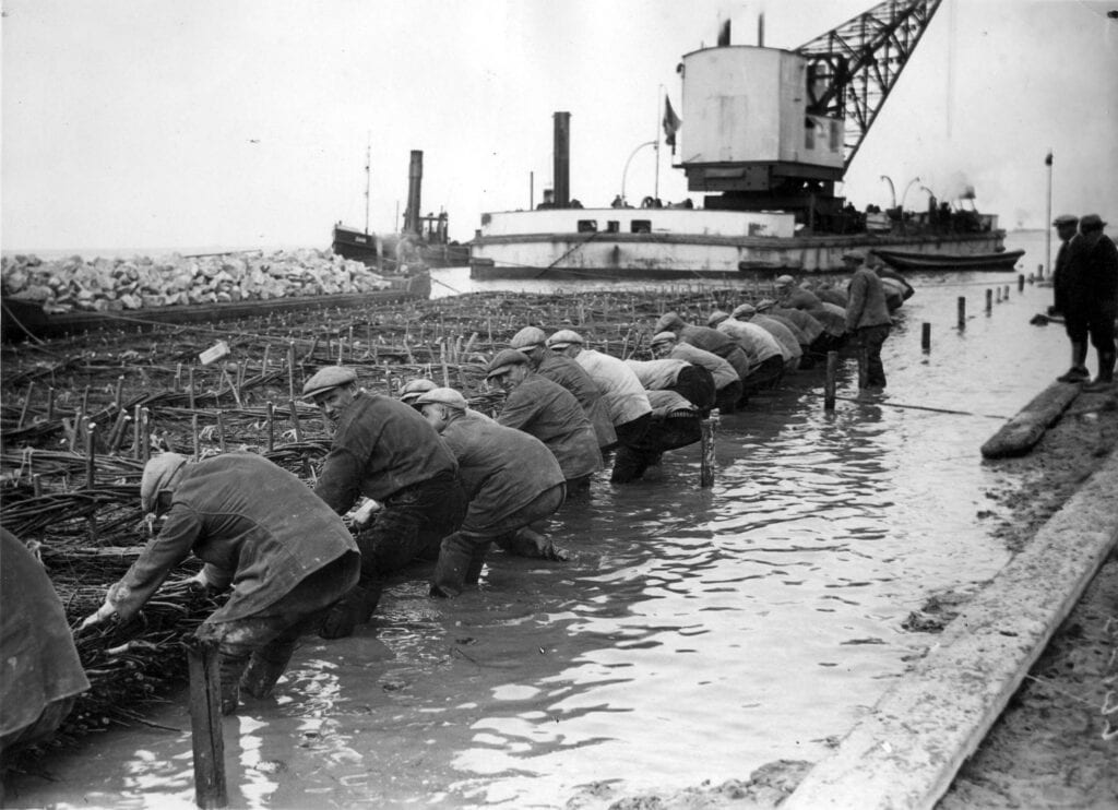 Aanleg van de Afsluitdijk. Arbeiders leggen het fundament van gevlochten wilgentenen, april 1932.