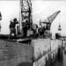 Arbeiders voeren betonmortel aan om kieren tussen de caissons van de Zandkreekdam mee te dichten, 3 mei 1960.