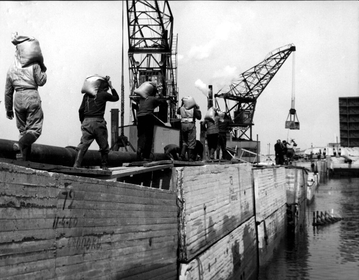 Arbeiders voeren betonmortel aan om kieren tussen de caissons van de Zandkreekdam mee te dichten, 3 mei 1960.